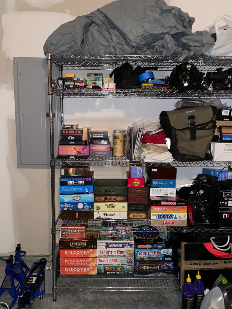 a metal shelf that has organized board games on one have and disorganized car parts on the other.
