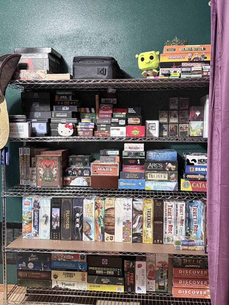 a shelf with more games, however the 2 shelf from the bottom now has all the board games vertical like a book shelf rather than stacked in piles like on the other shelves. the blankets and crocheting supplies are gone, and there are more games on the top shelf.
