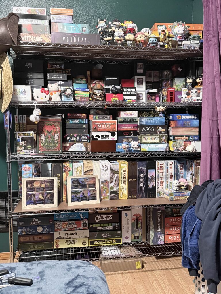 a shelf with more games. the top shelf now included more even more games, and funkos. There are various funkos sprinkled throughout the shelf and there are 2 card displays from the avatar the last airbender magic set.