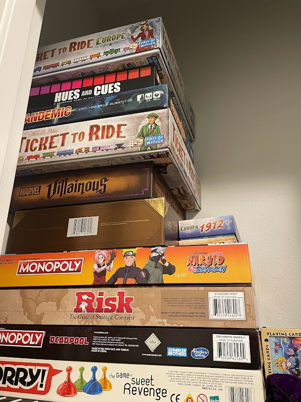 stack of board games on a shelf in a closest, from top to bottom:
ticket to ride europe
hues and cues
pandemic
ticket to ride
marvel villainous
box 1
both ticket to ride expansions
naruto monopoly
deadpool monopoly
sorry