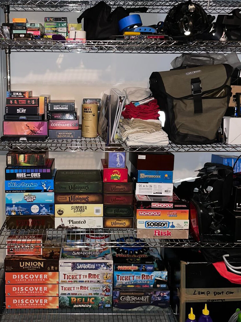 a metal shelf that has organized board games on one have and disorganized car parts on the other.